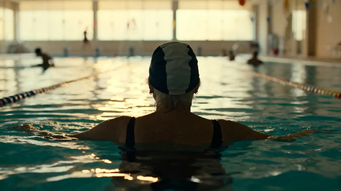 Femme senior flottant en piscine intérieure le matin